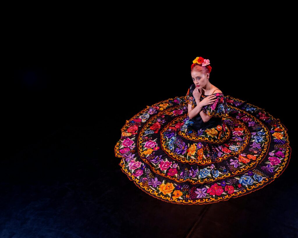 Woman in colorful Mexican folk dress performing traditional dance, captured from above.